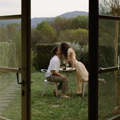 a man and woman sitting at a table in front of a window with an open door