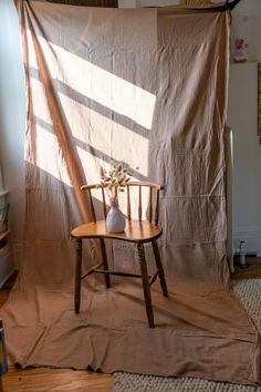 a chair sitting in front of a curtain with a vase on it's side