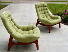 two green chairs sitting on top of a cement floor next to flowers and bushes in front of a house