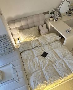 a white bed sitting next to a desk with a laptop on it's side