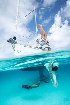 a man swimming in the ocean next to a sailboat and another person snuggling under water