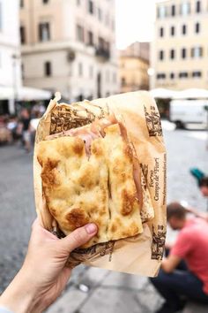 a person holding up a piece of food in front of some people on the street