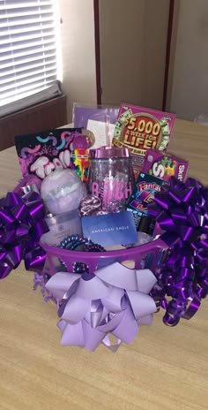 a purple basket filled with lots of different items on top of a wooden table next to a window