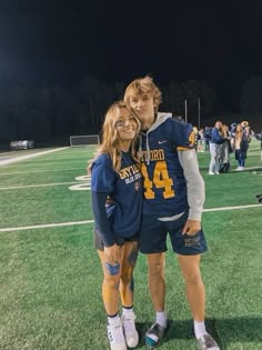 two young people standing on top of a football field at night with fans in the background