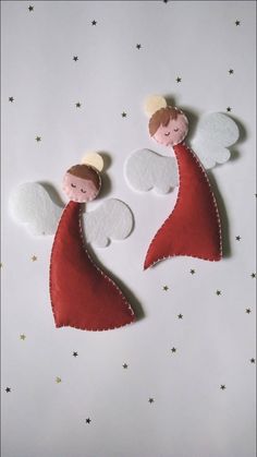 two felt angels with white wings and red cloaks on top of stars in the sky