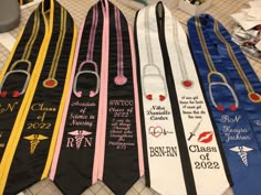 four graduation sashes are lined up on the floor with their names and designs printed on them