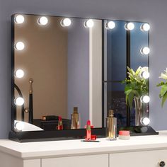 a white dresser topped with a large mirror and lights on it's sides next to a vase filled with flowers