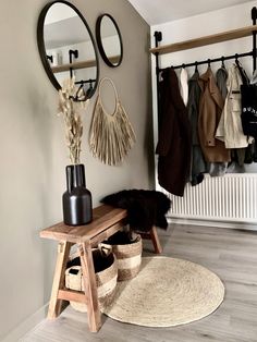 a wooden bench sitting under a mirror next to a coat rack filled with coats and hats