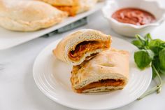 two pastries sitting on top of a white plate next to dipping sauce and basil leaves