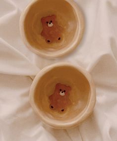 two brown bowls with teddy bears in them on a white cloth covered tablecloth, top view