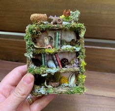 someone is holding a miniature book with plants and bookshelves on it in their hand