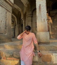 a man standing on some steps with his hand in his hair and wearing a pink shirt