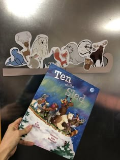 a person holding up a book in front of a refrigerator with magnets on it