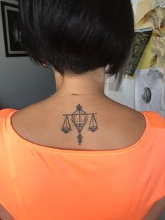 the back of a woman's neck with a libra symbol tattoo on it