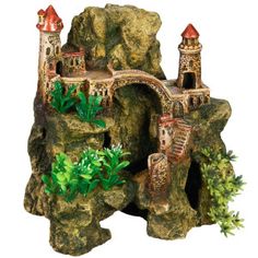 a toy castle with trees and bushes in front of the building on top of rocks