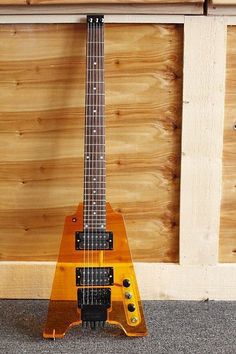 an orange electric guitar sitting on top of a wooden floor next to a wall with wood paneling