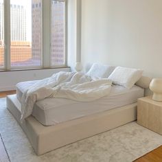 an unmade bed sitting in the middle of a room with a large window above it