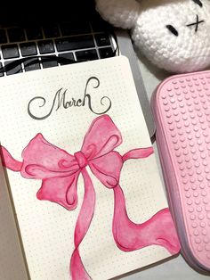 a notepad with a pink ribbon on it next to a teddy bear and pen