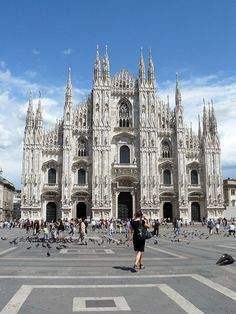 people are walking around in front of a large building with many spires and windows