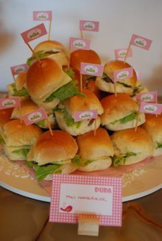 small sandwiches are arranged on a plate with little pink flags and place cards for name tags