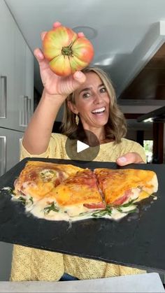 a woman holding an apple and pizza on a pan in her hand while smiling at the camera