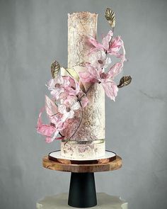 a three tiered wedding cake with pink flowers on the top and bottom, sitting on a wooden stand