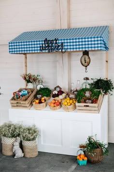 an outdoor market with fresh fruits and vegetables on display under a blue checkered awning