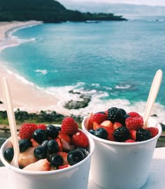 two cups filled with fruit sitting on top of a table next to the ocean and beach