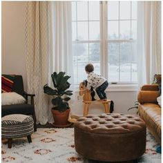 a young boy sitting on a stool in front of a window next to a couch