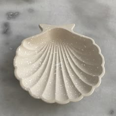 a white shell shaped dish sitting on top of a marble countertop next to a spoon