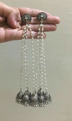 a hand holding three silver bells with pearls hanging from it's sides and two other beads attached to them