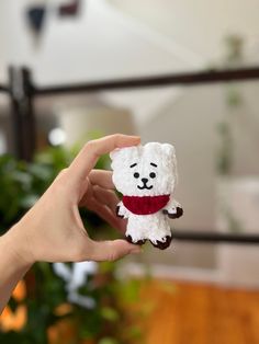 a hand holding a small white teddy bear with a red scarf around it's neck