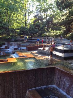 people are standing in the water at an outdoor park with many fountains and small waterfalls