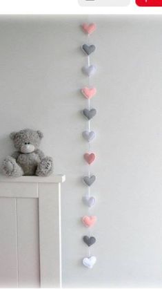 a teddy bear sitting on top of a dresser next to a wall hanging heart garland