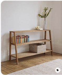 a wooden shelf with books on it next to a white rug and a vase filled with flowers