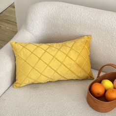 a basket filled with oranges sitting on top of a couch next to a pillow