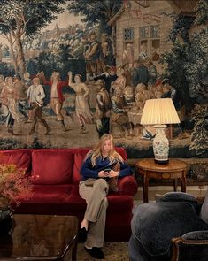 a man sitting on a red couch in front of a wall with paintings and lamps