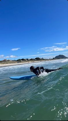 a person laying on a surfboard in the middle of the ocean with clear blue skies