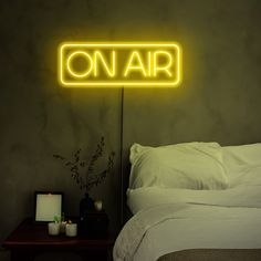 a neon sign that reads on air above a bed in a room with a night stand