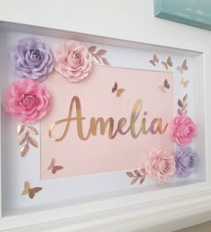 a white frame with pink, purple and yellow flowers on it that says amelie in gold lettering