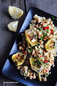 artichokes and rice on a black plate with lemon wedges