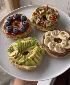 four different types of pastries on a white platter with blueberries, bananas and kiwi