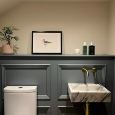 a white toilet sitting next to a bathroom sink under a framed picture on the wall