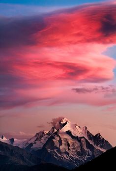 the mountains are covered in snow and clouds as the sun is setting on top of them