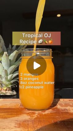 a jar filled with orange juice sitting on top of a wooden table next to a pineapple