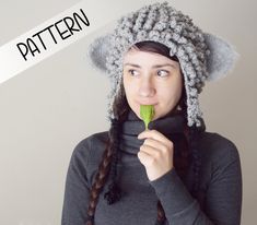 a woman wearing a knitted hat while holding a green object in her mouth