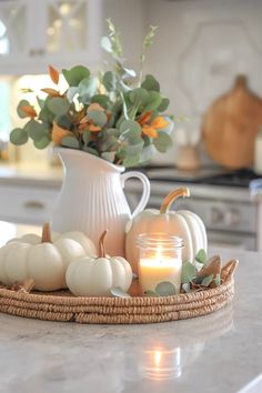 a white vase filled with pumpkins and greenery on top of a kitchen counter