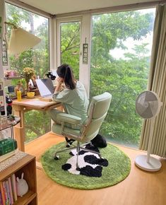 a woman sitting at a desk in front of a laptop computer on top of a green rug