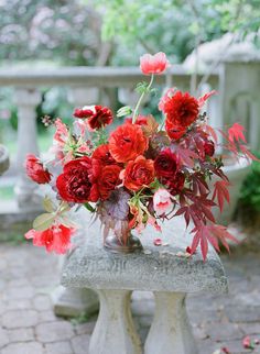 a vase filled with red flowers sitting on top of a cement bench