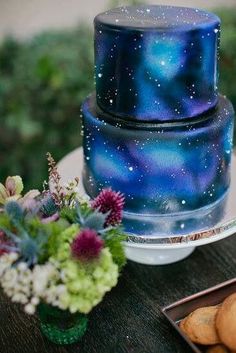 a blue cake sitting on top of a wooden table next to flowers and other items